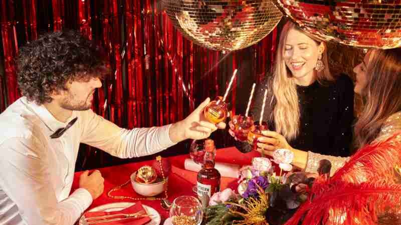 3 friends cheers with their Southern Comfort bauble drinks in a making merry party setting with disco balls and confetti
