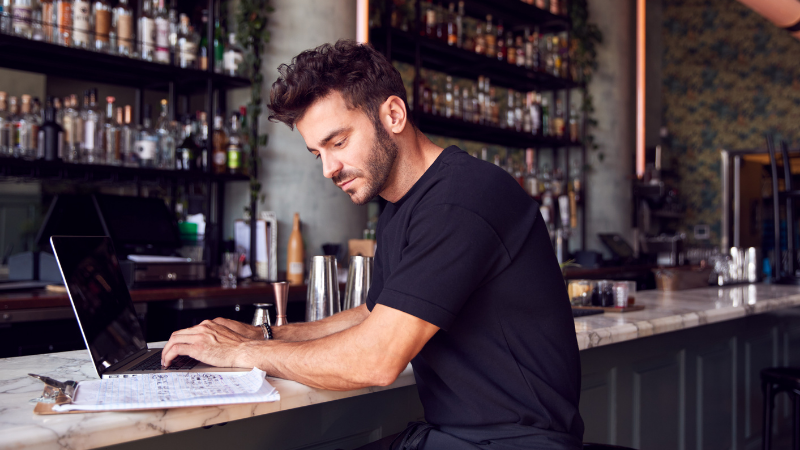 An Image Of A Man Using His Laptop In A Bar
