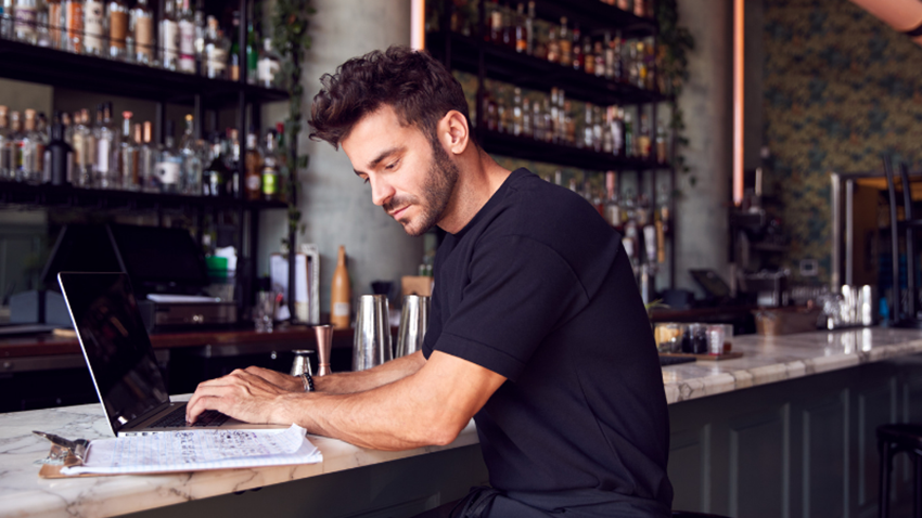 An Image Of A Man Using His Laptop In A Bar
